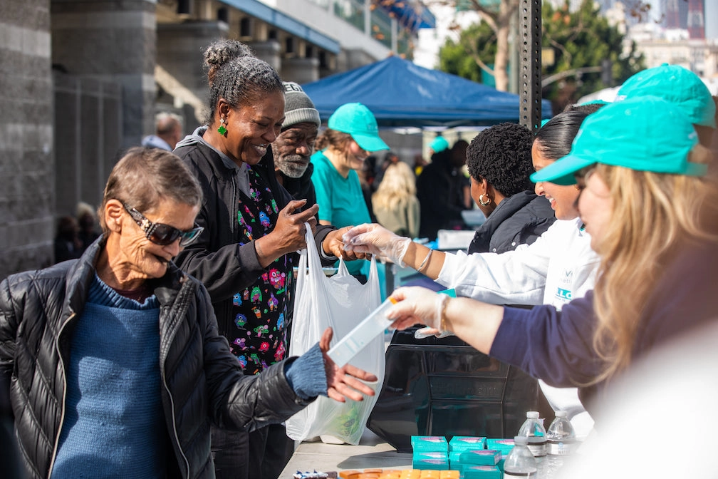 Volunteers in teal caps handing out products at an outdoor donation event