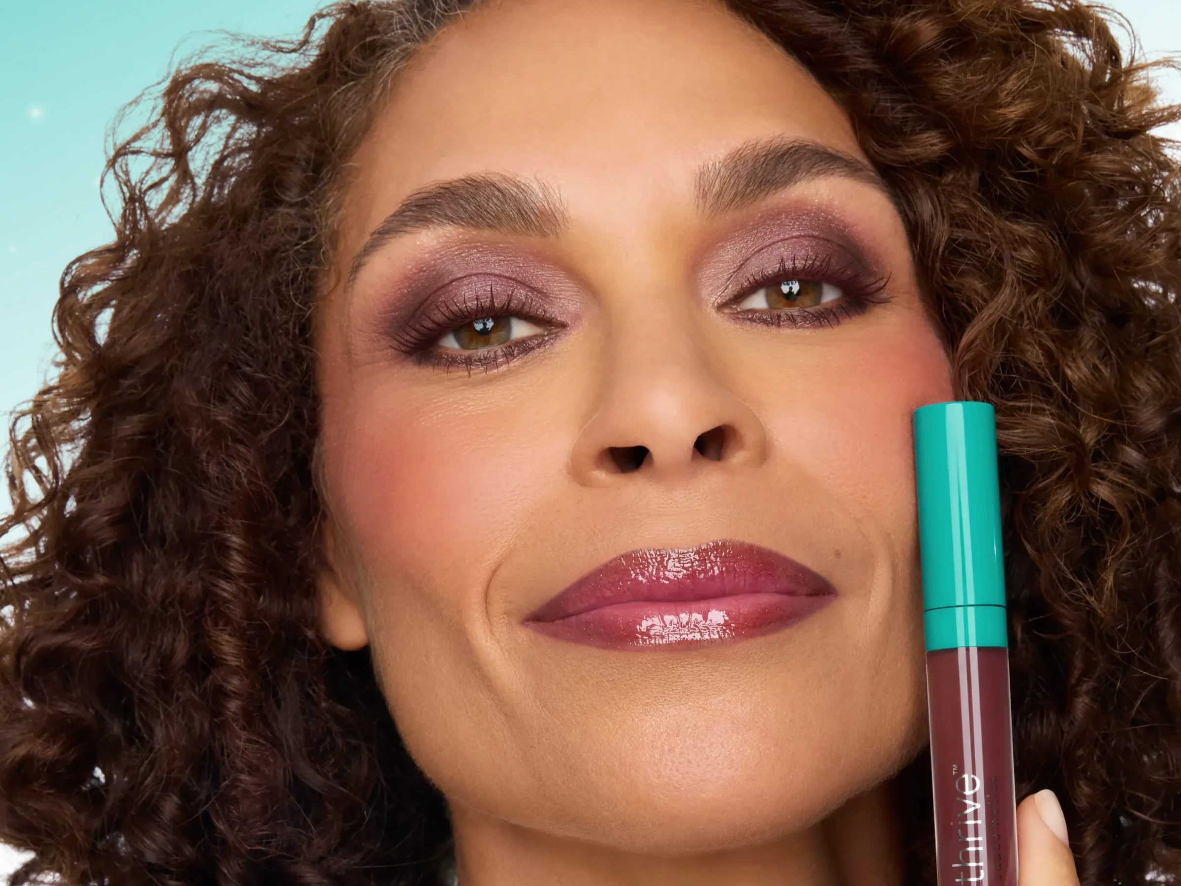 Woman wearing berry eye makeup and holding a turquoise stick to her cheek
