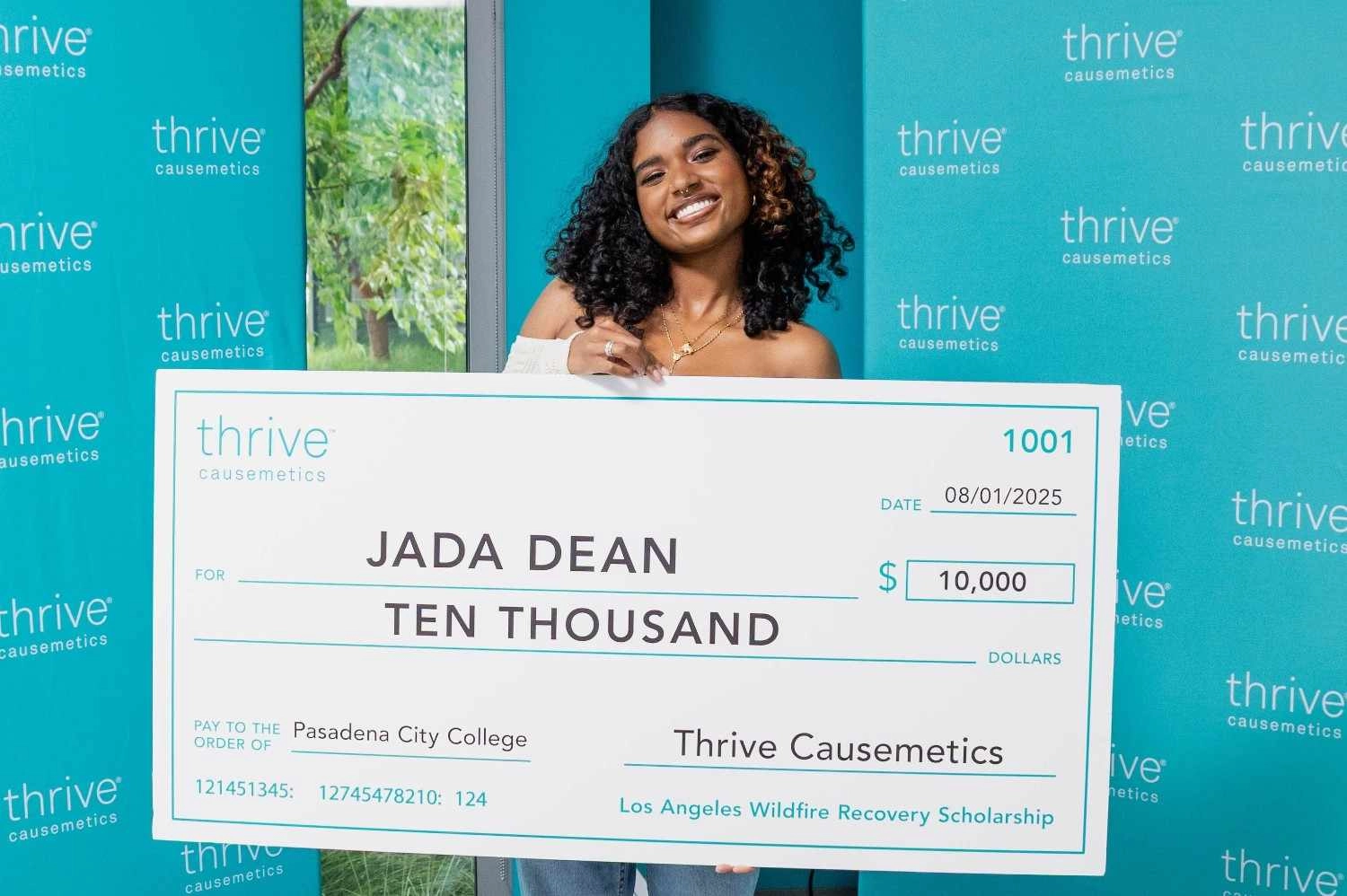 Woman standing behind a large Thrive Causemetics donation check