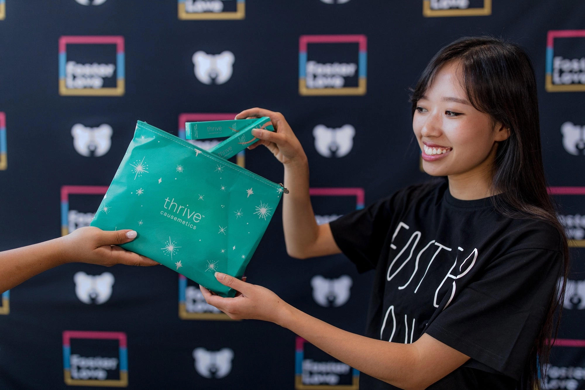 Woman smiling while receiving a teal cosmetic bag from another person